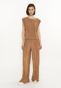 Top plié maro cu mâneci tip capac, asortat cu pantaloni largi plié. Textură moale, design fluid și croi lejer. Include adidași albi.