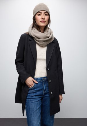 Zwarte wollen jas met een dubbelzijdig ontwerp, gecombineerd met een lichtbeige sjaal en hoed, gedragen over een crèmekleurige trui en blauwe jeans.