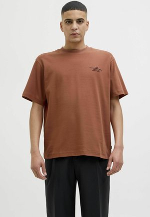 Himbeerfarbener Baumwoll-T-Shirt mit kurzen Ärmeln, Rundhalsausschnitt und kleinem schwarzen Schriftzug auf der Brust, kombiniert mit locker sitzenden dunklen Hosen.