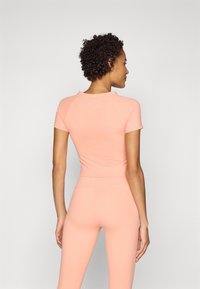 Helles rosa Sportoberteil mit kurzen Ärmeln und rundem Ausschnitt, kombiniert mit passender Leggings. Verfügt über dezente Markenkennzeichnung auf der Rückseite.