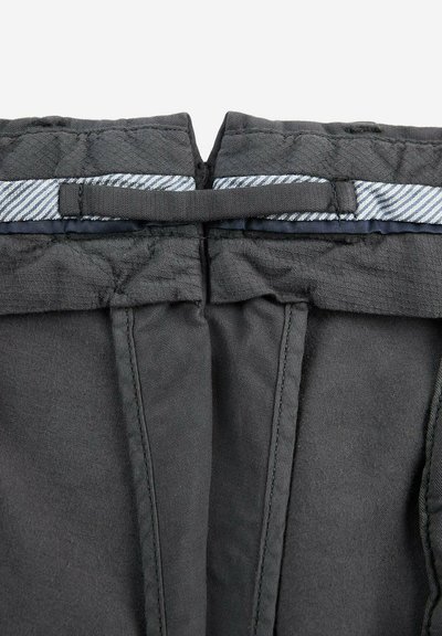 Tissu noir avec une finition texturée, présentant une ceinture rayée bleu et blanc. Comprend des coutures et des bretelles ajustables pour un ajustement optimal.