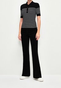 Polo à manches courtes rayé noir et blanc avec un col à boutons, assorti à un pantalon évasé noir et des baskets blanches.