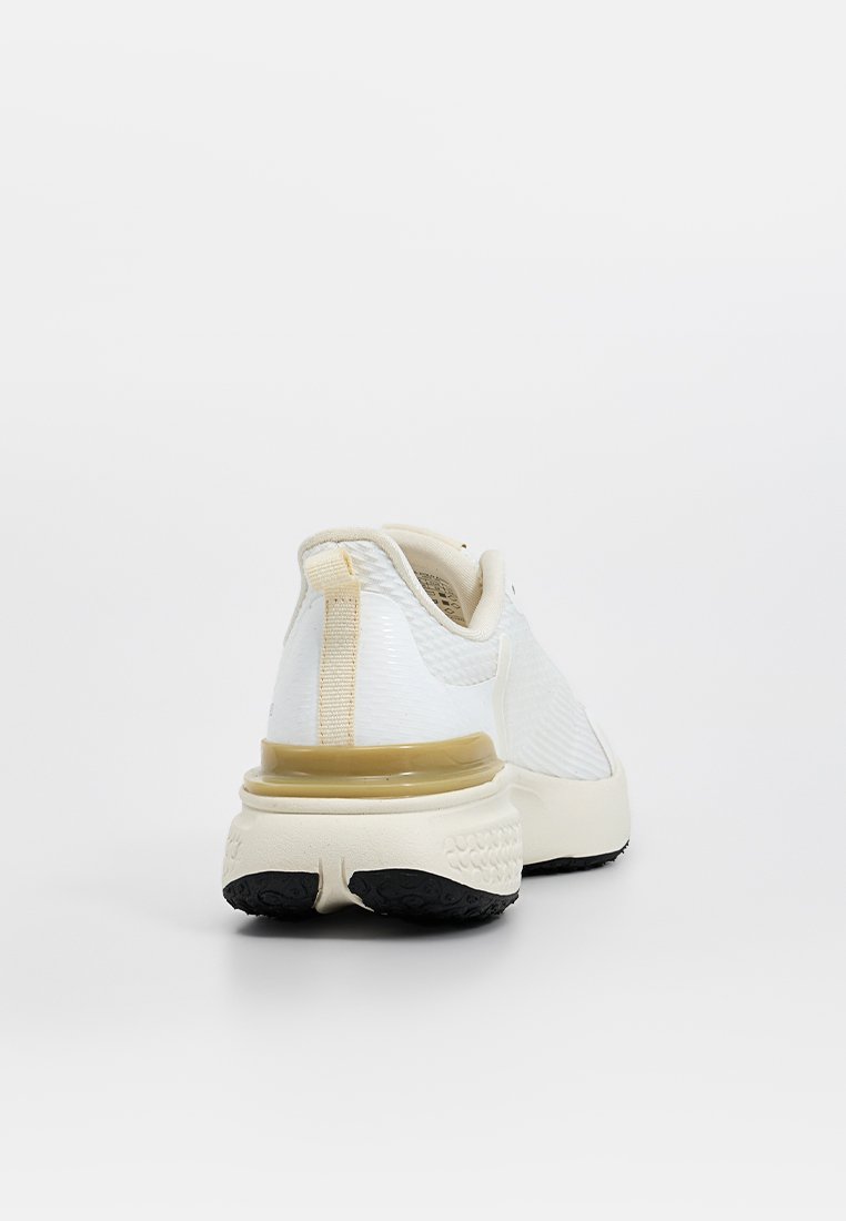 Zapatilla deportiva blanca con parte superior texturizada, acentos en beige contrastantes, amortiguación visible en el talón y suela de goma negra para tracción.