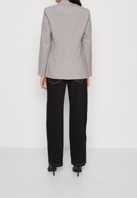 Harmaa bleiseri, jossa on istuva selkäosa, yhdistettynä mustiin leveisiin housuihin, joissa on erottuva valkoinen ommel, sekä mustiin korkokenkiin.