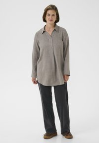 Camicia a maniche lunghe con colletto in tessuto beige chiaro lavorato, abbinata a pantaloni grigi scuri e scarpe marroni. Design semplice e rilassato.