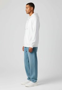 Felpa bianca con cappuccio e lacci, abbinata a jeans in denim blu chiaro e sneaker bianche. Design semplice, vestibilità rilassata e texture liscia.