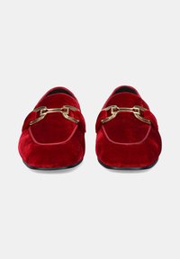 Zapatillas de terciopelo rojo sin cordones con una cadena decorativa dorada brillante en la parte frontal. Punta redonda y textura suave, con una suela negra.