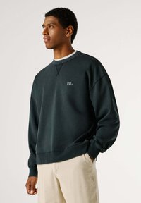 Felpa verde scuro con scollo a girocollo e logo ricamato "PJL". Tessuto a trama e vestibilità rilassata, abbinata a pantaloni leggeri a costine.