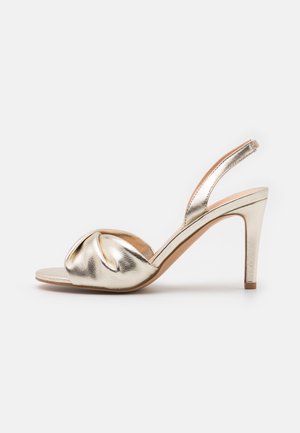 Sandale à talons hauts en métal doré avec un dessus noué, un design à bout ouvert et une bride de cheville. Elle présente une texture lisse et un talon élancé.