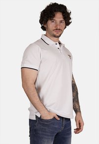 Polo bianco con colletto nero a trim, patta con due bottoni e dettaglio ricamato sul petto sinistro, abbinato a jeans in denim blu.