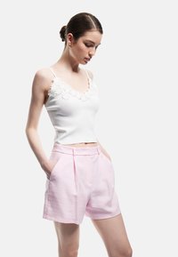 Witte mouwloze top met bloemenborduursel bij de halslijn, gecombineerd met lichtroze hoge shorts met zijzakken en plooien.
