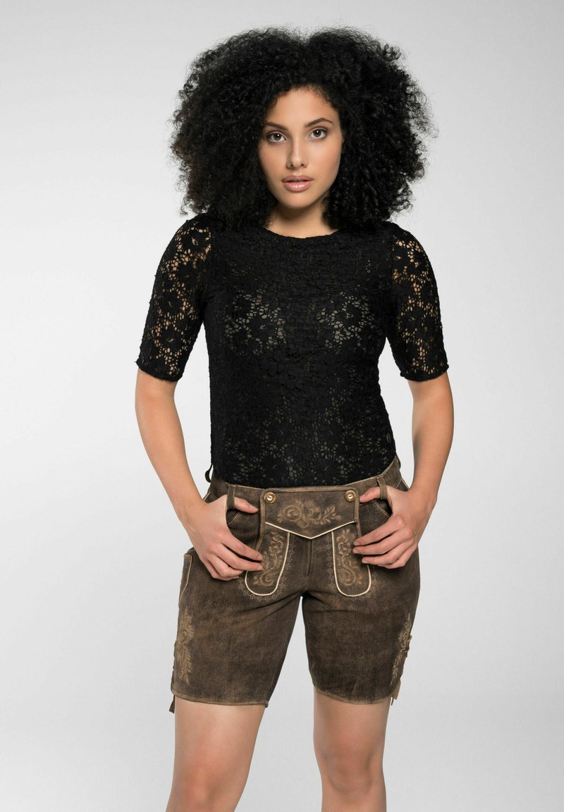 Schwarzes Spitzentop mit kurzen Ärmeln, kombiniert mit brauner Lederhose, die mit dekorativen Nähten und zwei seitlichen Taschen versehen ist. Insgesamt glatte Textur.