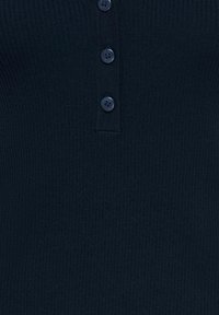 Gros plan sur une chemise en tissu côtelé foncé avec une patte de boutonnage ornée de quatre boutons noirs ronds, espacés de manière égale.