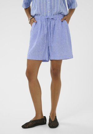 Person iført løse lyseblå linnedshorts med snøre, en blå- og hvidstribet skjorte og sorte vævede slip-on sko.