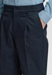 Navy trousers with a flat front, pockets on the sides, and an elastic waistband. Made from smooth fabric with a tailored fit.