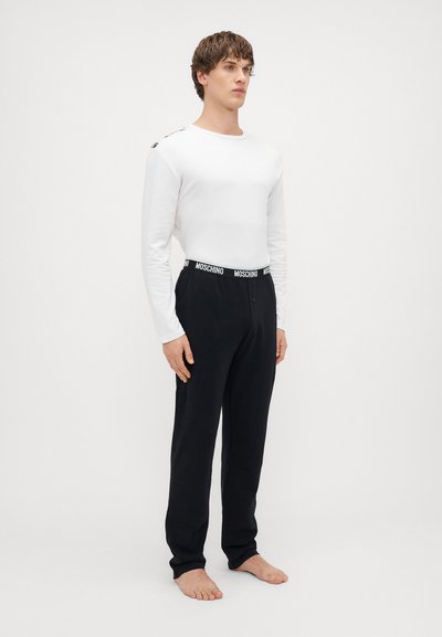 Pikkade varrukatega valge särk, mida täiendavad mustad püksid, millel on bränditud elastne piht. Riietus näitab lihtsat ja igapäevast disaini.