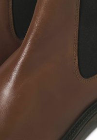Bottes de cheville en cuir marron avec des panneaux élastiques sur les côtés, texture lisse, détails noirs et couture contrastante le long de la semelle.