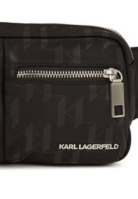 Marsupio in nylon nero con un motivo testurizzato, tasca con zip argentata e dettaglio del logo. Presenta un design elegante e compatto, adatto per un uso casual.