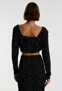 Zwart twee-delig outfit gemaakt van textuurstof met witte stippen; heeft lange mouwen, een cropped top en een high-waisted rok.