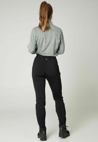 Zwarte sportbroek met een hoge taille en taps toelopende pijpen, gecombineerd met een lichtgrijs shirt met lange mouwen voorzien van een kraag en een gestructureerde stof.