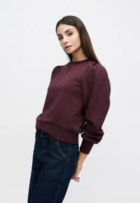 Vinrød genser med rund hals og puffede ermer, laget av bomullsblanding, med ribbestrikkede mansjetter og kant, kombinert med mørkeblå denimjeans.