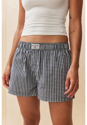Kvinde iført sort-hvide ternede shorts med BDG Jeans mærke og hvid cropped tanktop, der viser maven.