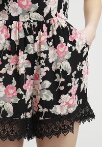 Blommig svart rompers med rosa och krämfärgade blommor; samlad midja, sidofickor och svart spetskant vid fållen. Lättviktig tyg.