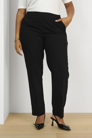 Zwarte op maat gemaakte broek met een gladde textuur, hoge taille, zijzakken en taps toelopende benen, gecombineerd met zwarte pumps met een spitse neus.