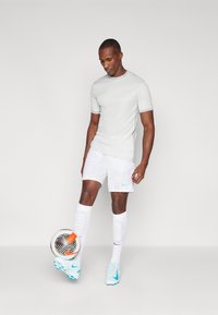 Camiseta deportiva Nike de color gris claro con detalles en azul verdoso, combinada con pantalones cortos gris claro con rayas verticales, calcetines blancos y zapatillas de color azul claro.