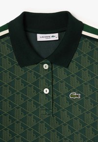Grön pikétröja med ett geometriskt mönster, ribbad krage, två vita knappar och broderad krokodil-logga. Slim fit stil.