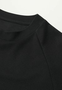 Tissu noir texturé avec un col rond et des manches raglan, présentant des détails de couture fines. Convient pour un usage décontracté ou en superposition.