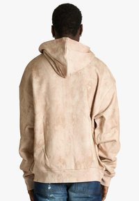 Sweat à capuche surdimensionné couleur sable avec une finition texturée, doté d'une capuche et d'un ourlet côtelé. Vue de dos, mettant en avant des épaules tombantes et un design décontracté.