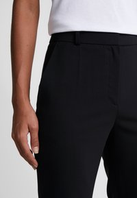 Sukně z černého materiálu s hladkou texturou, rovný střih a nažehlené záhyby; plochý přední díl s bočními kapsami a nenápadným pasem.