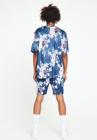 Marinblå polyester-set med blomstertryck över hela. Kortärmad topp och matchande shorts. Slät textur, avslappnad passform, med vita träningsstrumpor och sneakers.