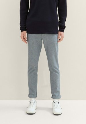 Pantalons slim gris en tissu texturé, avec des ourlets retroussés, associés à des baskets blanches et à un haut à manches longues bleu marine.