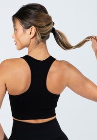 Zwarte geribbelde sporttanktop met een racerback ontwerp. De stof heeft een gestructureerde uitstraling en de top heeft een cropped pasvorm net onder de taille.