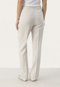 Pantaloni beige chiaro su misura con vestibilità dritta, due tasche posteriori e una texture del tessuto liscia. Completati con scarpe argento piatte.