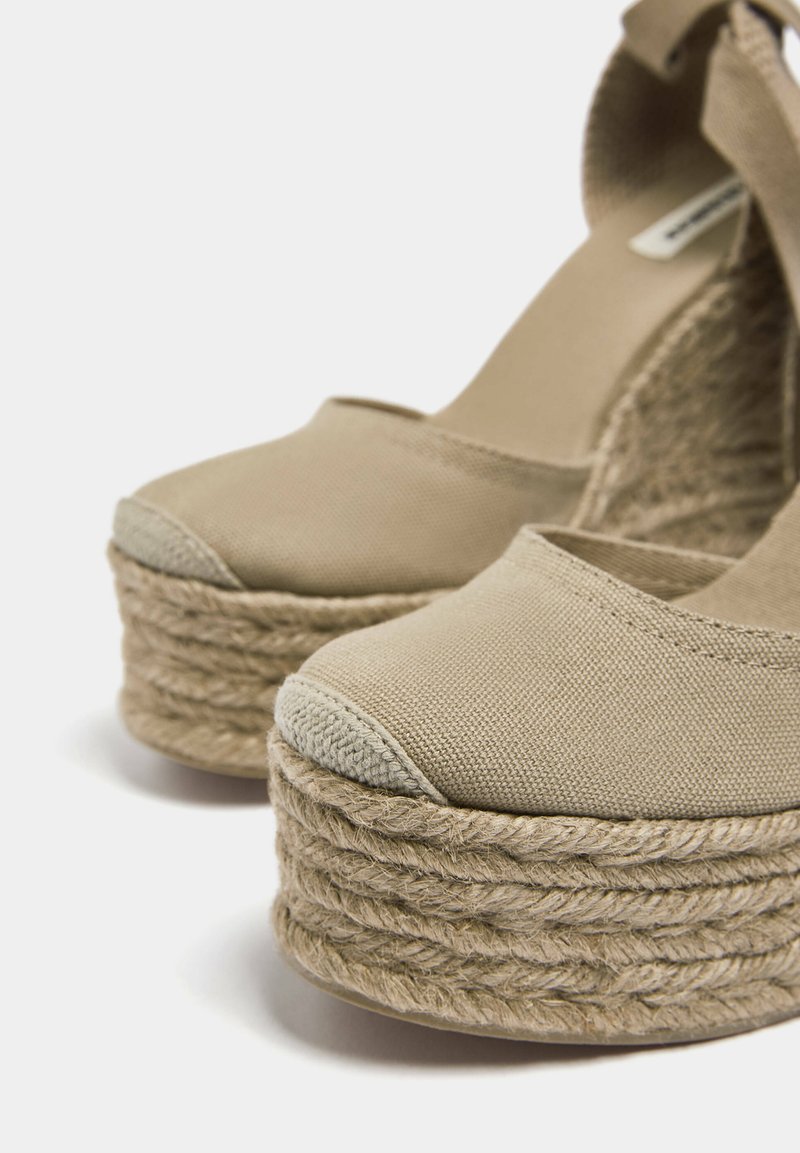 Beige Leinenschuhe mit Keilabsatz und geflochtenen Jutesohlen sowie einer runden Zehenpartie. Verfügt über ein strukturiertes Obermaterial und ein elastisches Knöchelriemchen.