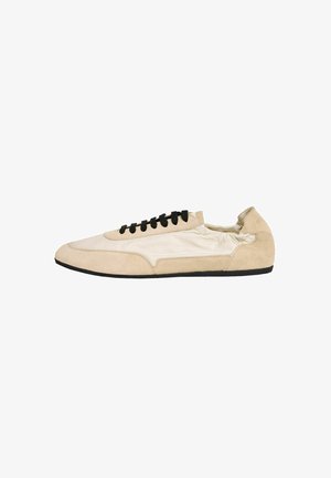 Beige og creme lav-top sneakers med sorte snørebånd og en sort sål, fremstillet af ruskind og stofmaterialer, vist i sideprofil.