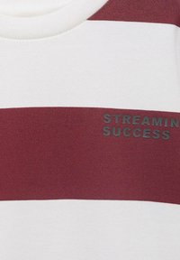 Pruhované tričko v striedajúcich sa marhuľových a bielych farbách, s jemnou textúrou látky a s nápisom "STREAMING SUCCESS" embosovaným čiernou farbou na prednej strane.