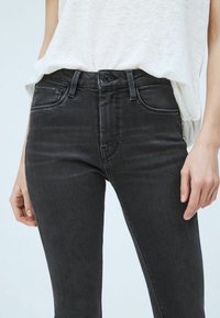 Jeans de mezclilla negra con un diseño ajustado, estilo de cinco bolsillos, trabillas para cinturón y un ligero desvanecimiento. El material es suave y con un ligero estiramiento.