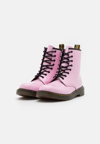 Stivali in pelle verniciata rosa con lacci neri e branding giallo sul tallone. Punta rotonda e suole in gomma nera con dettagli di cucitura.