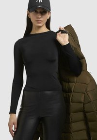 Sort langærmet top sammen med skinnende sorte leggings, holder en olivengrøn puffjakke med quiltet tekstur og tætsiddende design.