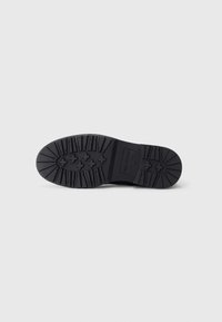 Black rubber sole with a textured tread pattern, featuring circular and linear designs for grip and durability. Minimal branding on the side.