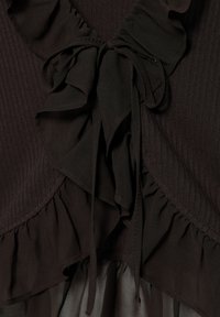 Tessuto ribbed marrone scuro con strati di volant e un dettaglio a fiocco legato al centro, che mostra texture e cuciture da vicino.