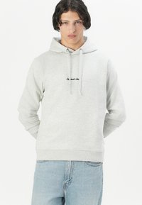 Felpa grigia realizzata in morbido misto cotone, con tasca frontale e cappuccio con cordino, caratterizzata da testo ricamato sul petto. Polsini fitted.
