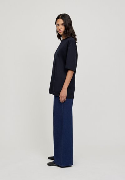 T-shirt en coton oversize bleu marine avec des manches courtes, associé à un pantalon en denim taille haute et à coupe large de couleur bleu foncé. Design simple, sans motifs visibles.