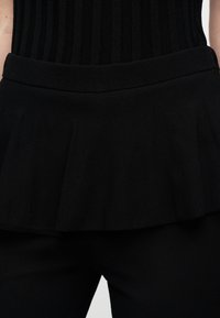 Μαύρο τοπ με ριμπ υφή και φαρδιά peplum σχεδίαση, με επίπεδη ζώνη στη μέση. Το ύφασμα είναι λείο και ελαστικό.