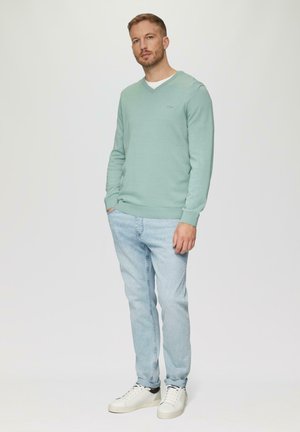 Lichtgroene v-hals trui met geribbelde manchetten en zoom, gecombineerd met lichtblauwe jeans en witte sneakers. Eenvoudig ontwerp, geen patronen.