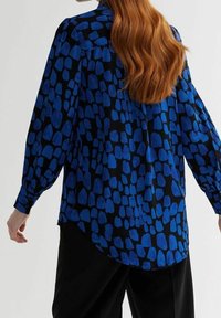 Long-sleeve blouse featuring a blue and black abstract pattern, made from lightweight fabric with buttoned cuffs and a curved hem.